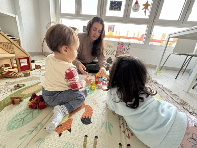 Alba con dos niños en la madre de día pequecuario en Alicante jugnado a construir con bloques.